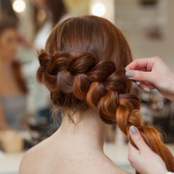Beautiful, with long, red-haired hairy girl, hairdresser weaves a French braid, close-up in a beauty salon. Professional hair care and creating hairstyles.